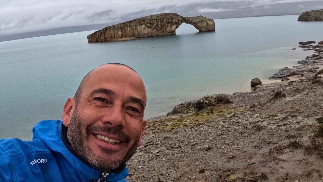 Selfie de Tomykat frente al Lago Posadas con puente de roca y camper 4x4 durante ruta overland