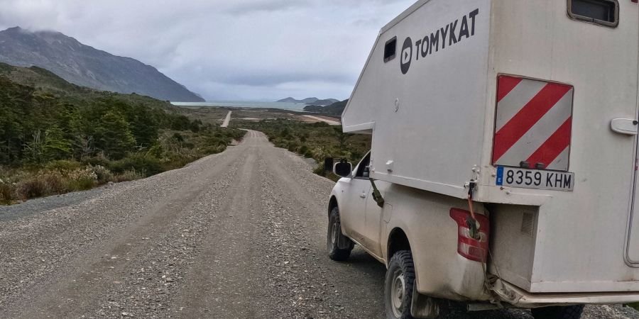 vehículo Overland 4x4 junto al cartel de Tierra del Fuego, Chile, con paisaje austral y viento fuerte