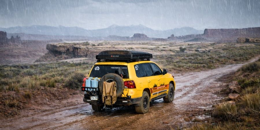 Vehículo overland circulando por pista de tierra en paisaje abierto de montaña lloviendo